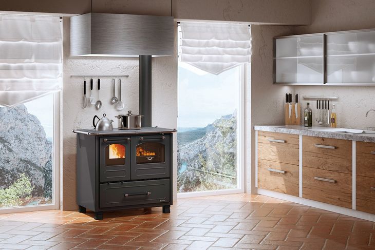 Cucina moderna con stufa a legna accesa, elettrodomestici in acciaio inossidabile e ampie finestre con vista su un paesaggio innevato.