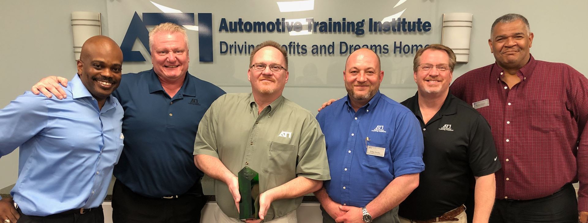 A group of men are posing for a picture in front of a sign that says automotive training institute.