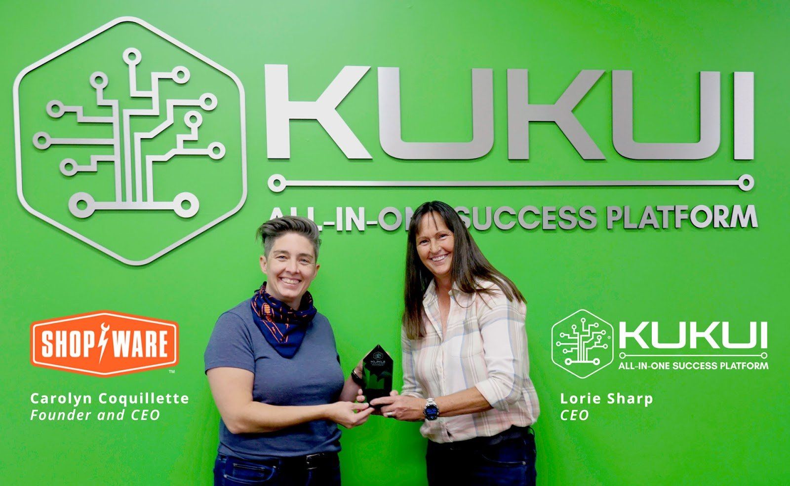 Two women are standing next to each other in front of a green wall.