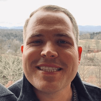 A close up of a man 's face smiling with mountains in the background.