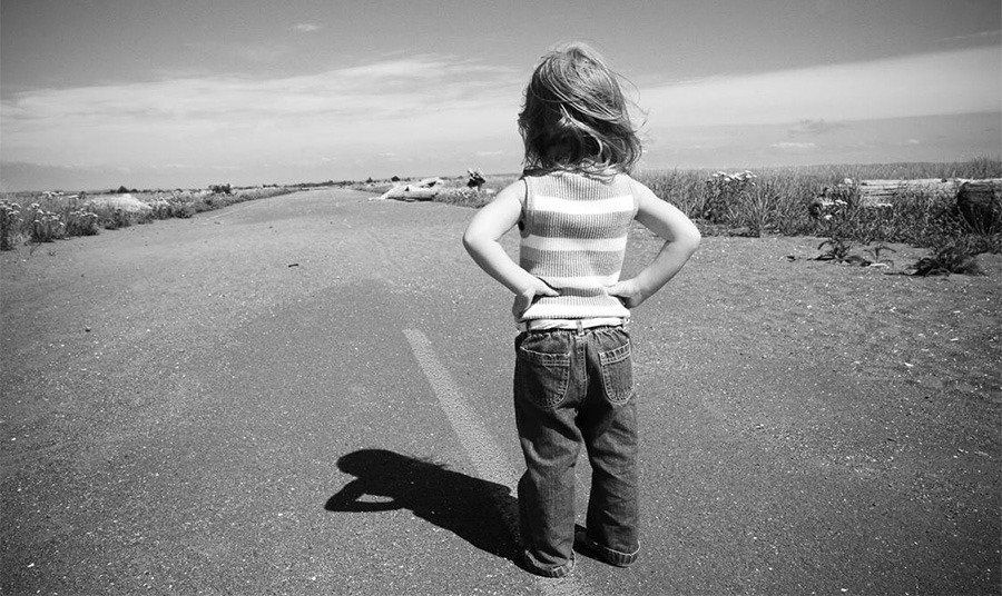 A little girl is standing on the side of a road with her hands on her hips.