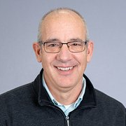 A man wearing glasses and a sweater is smiling for the camera.