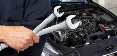 A man is holding two wrenches in front of a car.