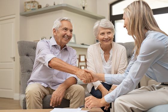 An elderly couple is shaking hands with a woman while sitting on a couch.