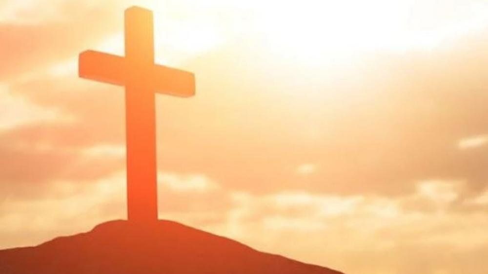 A cross is sitting on top of a hill at sunset.