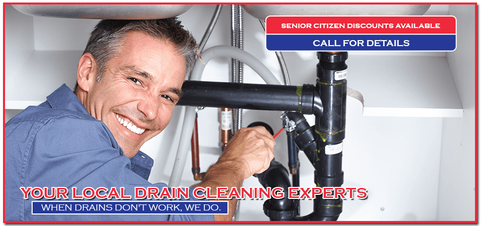 Plumber smiling while working on pipes under a sink; advertisement for drain cleaning services.