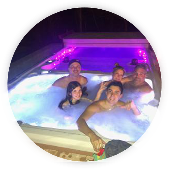 People smiling in a hot tub lit with purple lights at night.