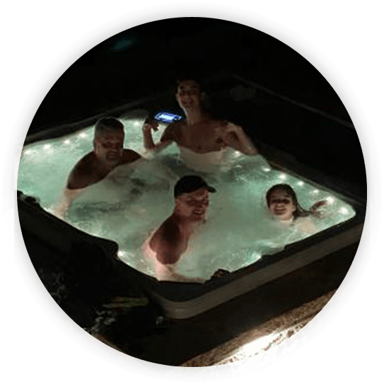 Four people relaxing in a lit hot tub at night, smiling.