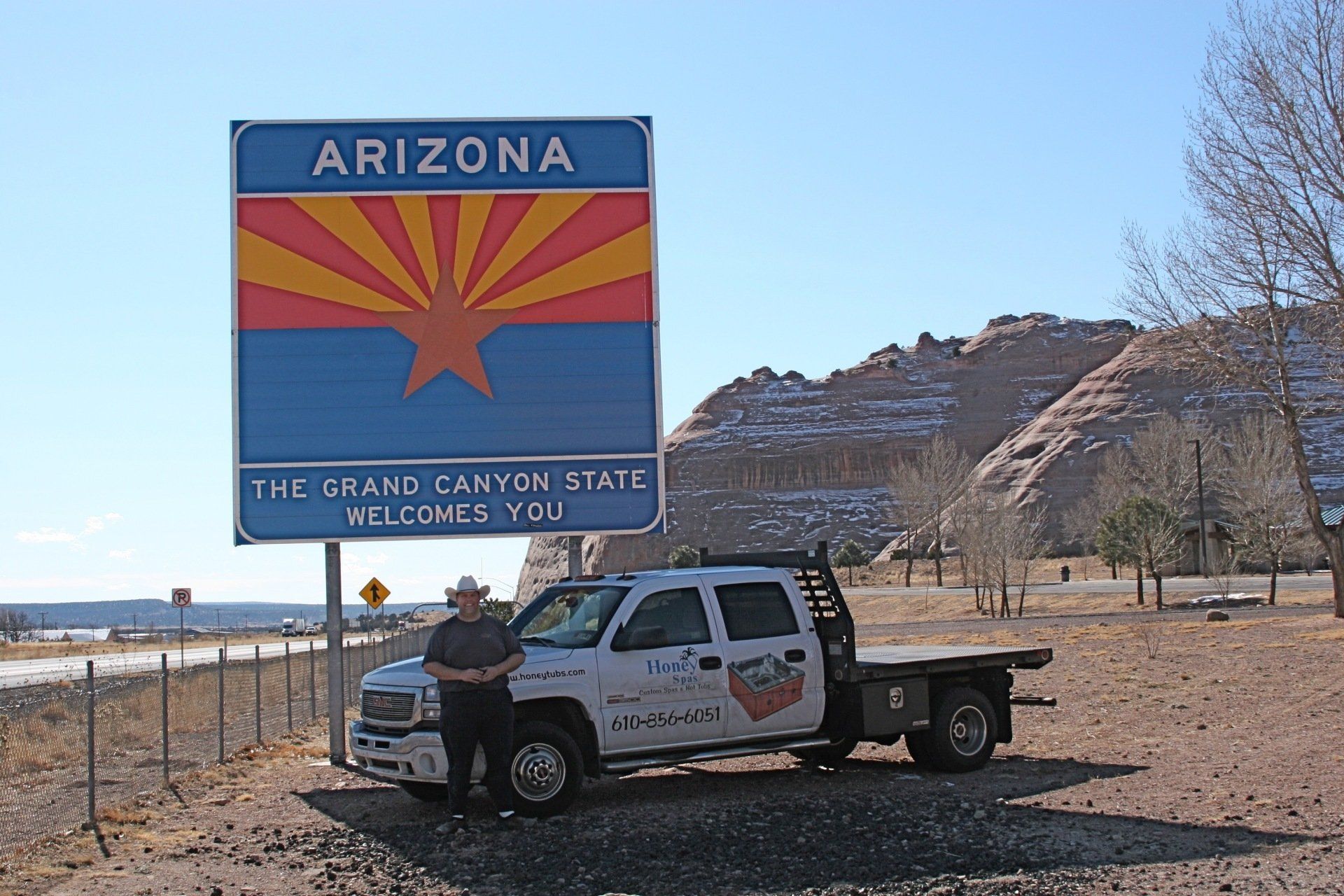 Man standing next to a truck with an Arizona state sign in front of a desert landscape.