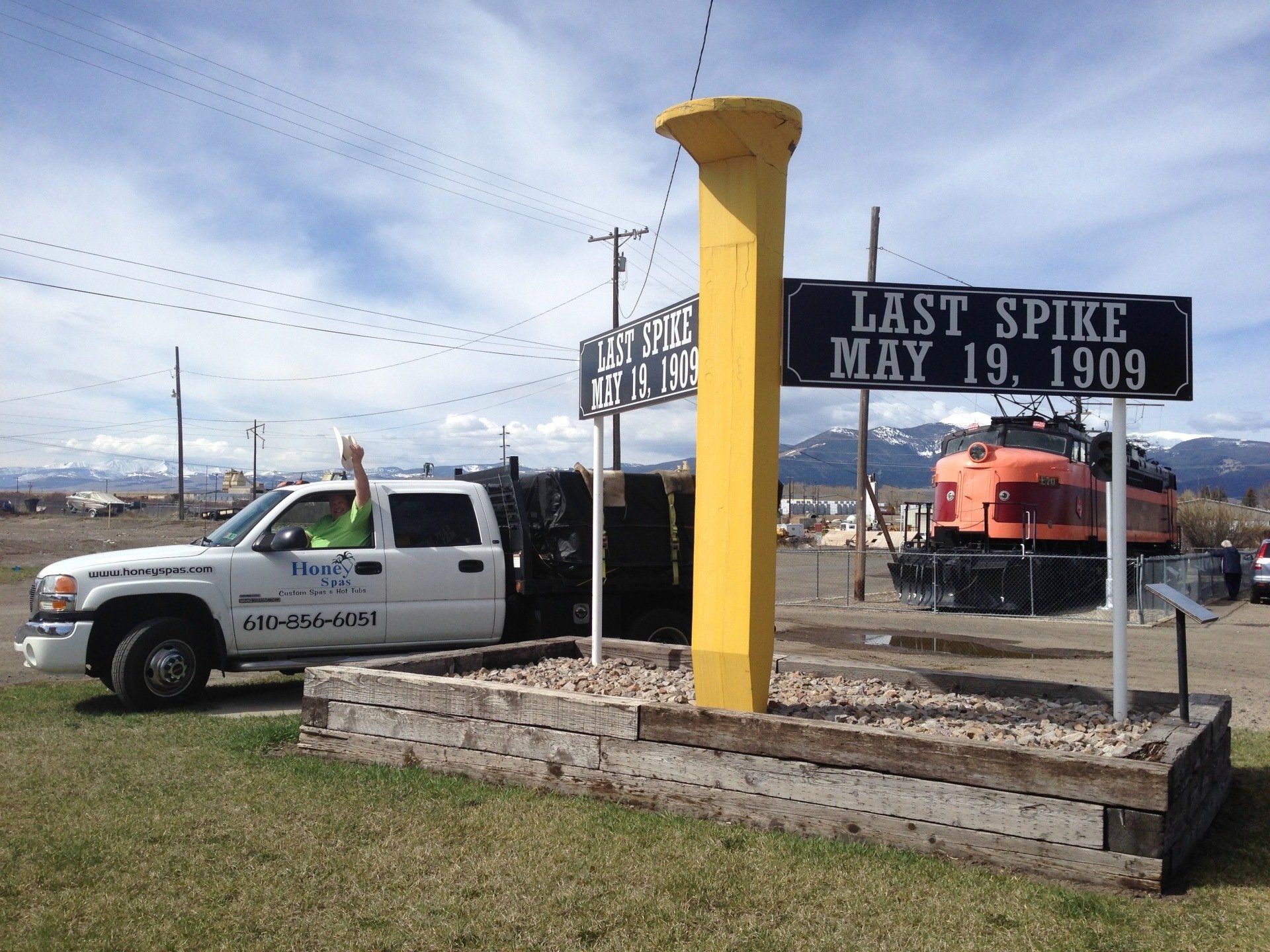A white truck near a yellow sculpture of a spike that commemorates the Last Spike, May 19, 1909.