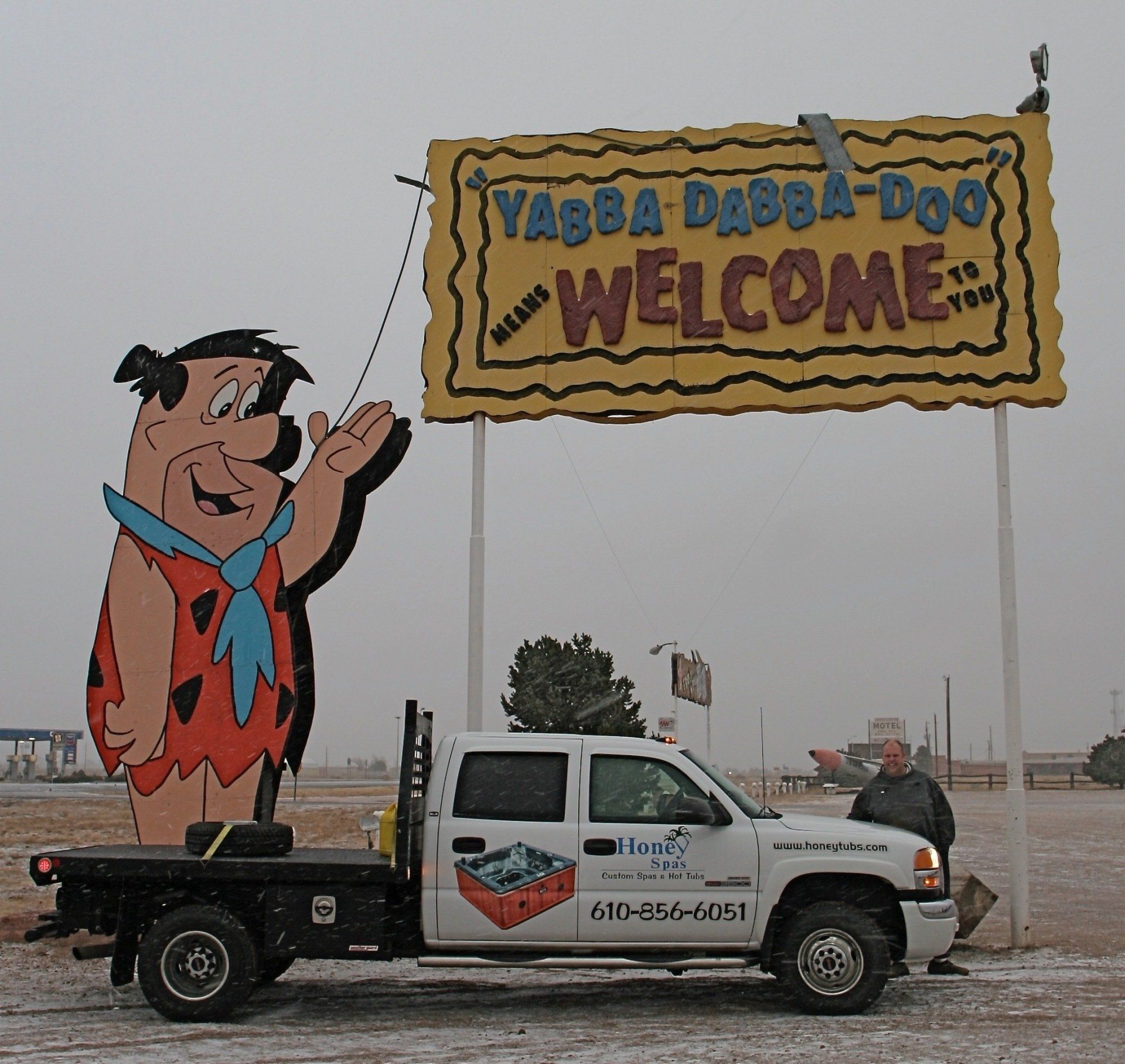 Fred Flintstone welcomes visitors with a sign. A flatbed truck parked nearby.