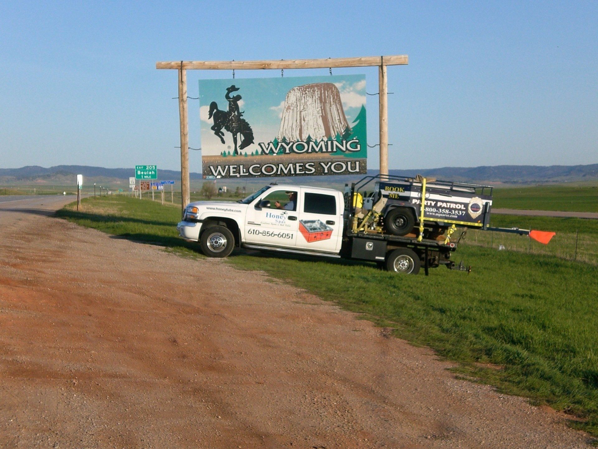 White truck in Wyoming, under state welcome sign, featuring a cowboy on a horse.