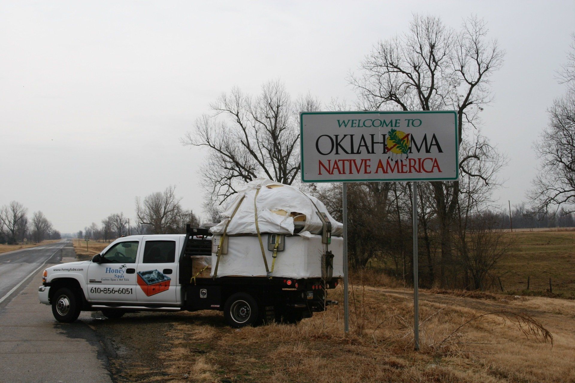 Truck parked near Oklahoma welcome sign, hauling a covered load on an overcast day.