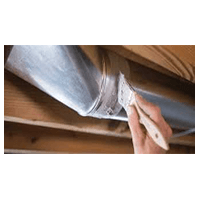 Hand scraping white paint from a silver metal duct in a wooden structure