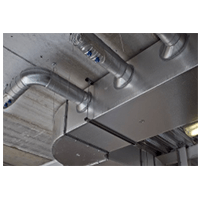 Metal HVAC ductwork and piping running along an industrial ceiling.
