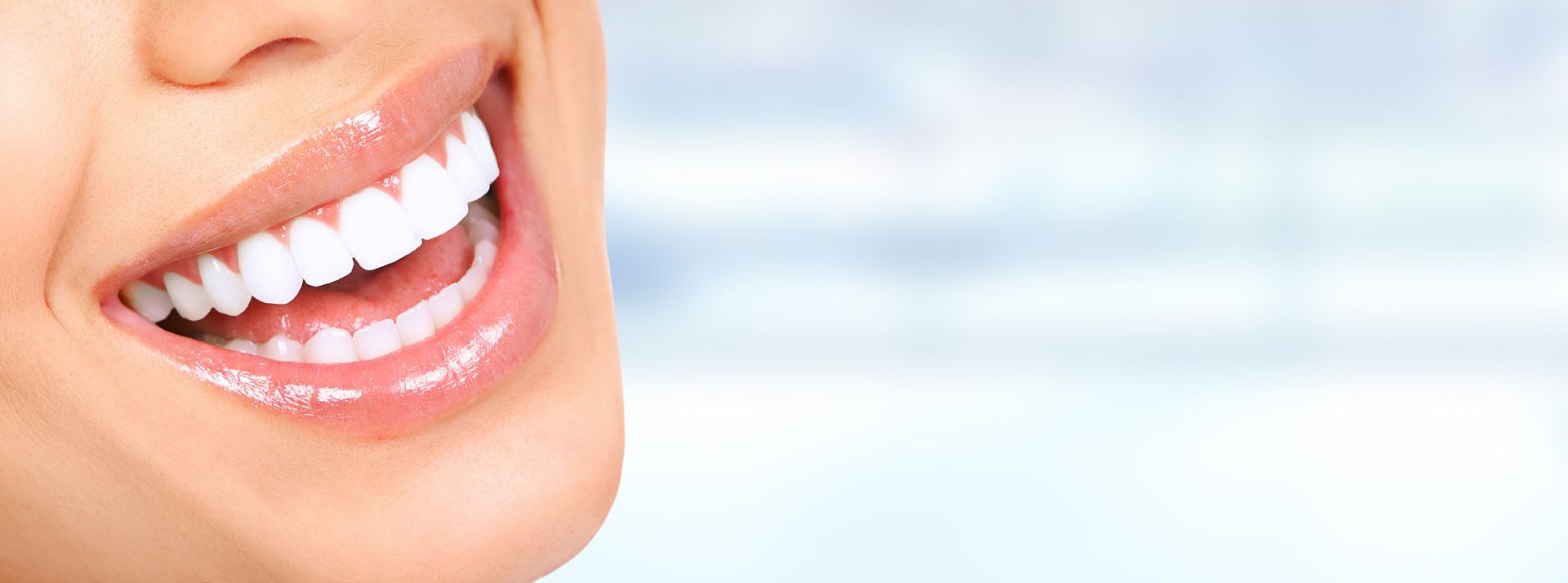 Primo piano di una bocca sorridente con denti bianchissimi su uno sfondo azzurro tenue.