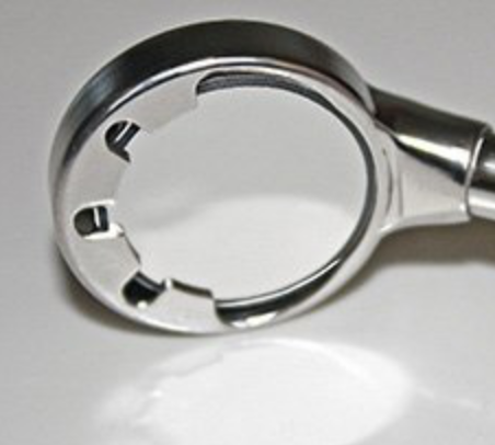 Close-up of a silver ratchet wrench head with openings for sockets, resting on a white surface.