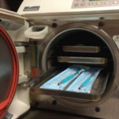 Sterilizer with trays of packaged dental instruments; open door, metal casing.