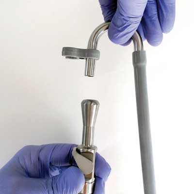 Hands in blue gloves connecting medical device components, a curved metal tube and handle.