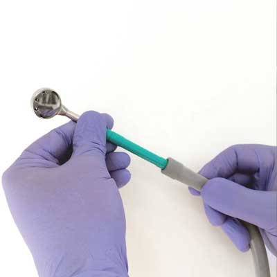 Hands in purple gloves holding a dental tool with a metallic head and green and gray handle.