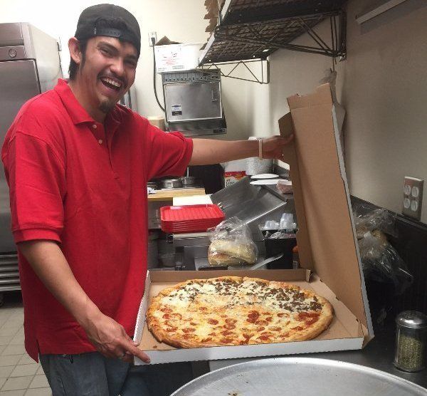 A man in a red shirt is holding a pizza in a box