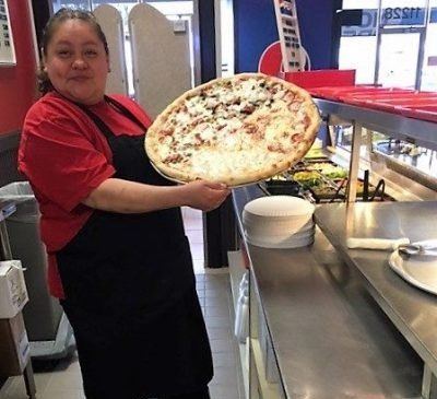 A woman in an apron is holding a pizza in her hands