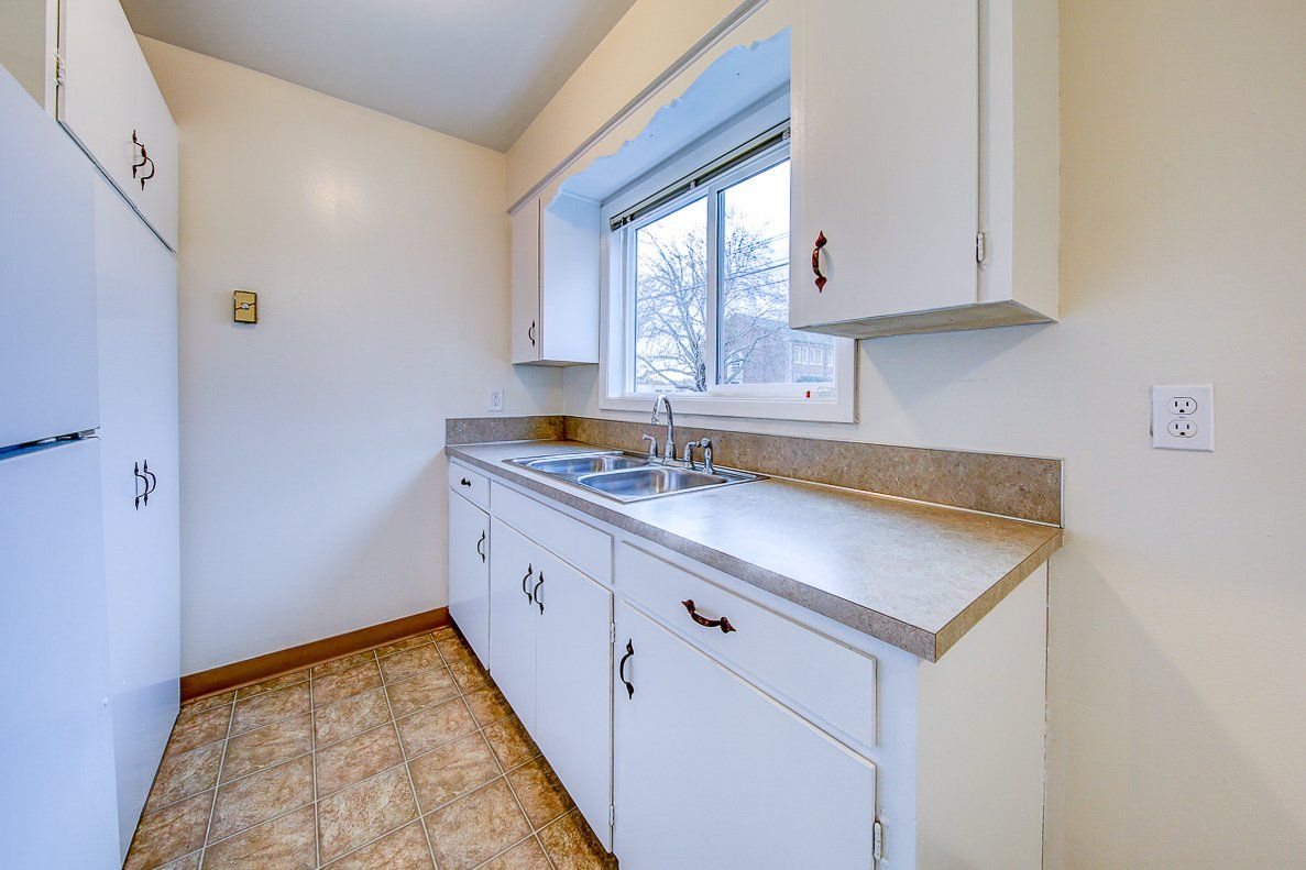 A kitchen with white cabinets , a sink , a refrigerator and a window.
