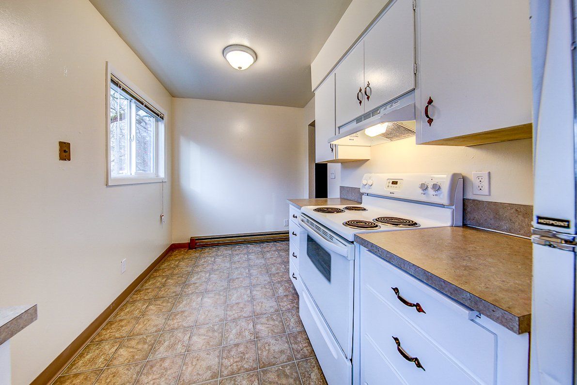An empty kitchen with white cabinets , a stove , and a refrigerator.