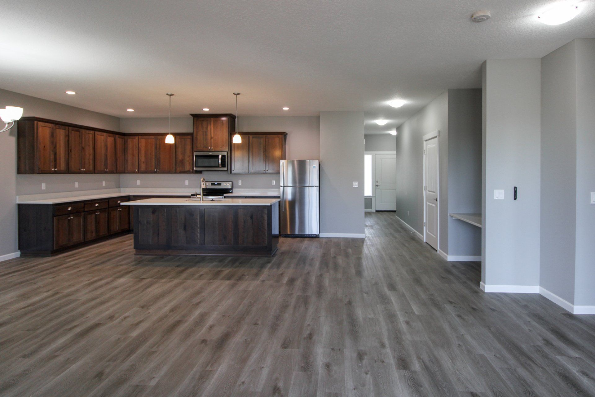 An empty kitchen in a house with hardwood floors and stainless steel appliances.