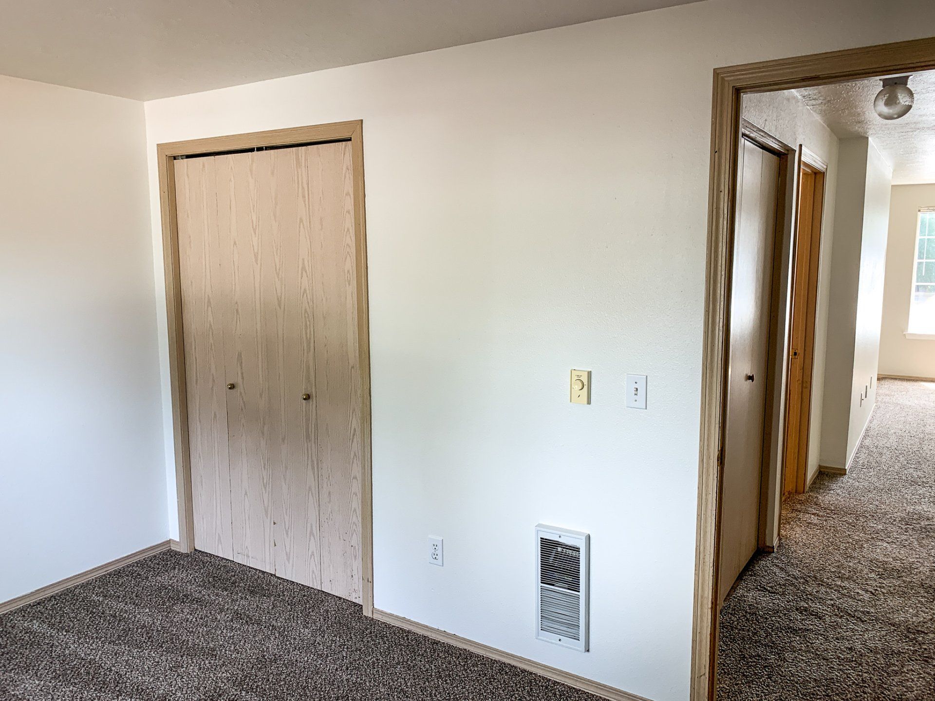 An empty room with a closet and a window.