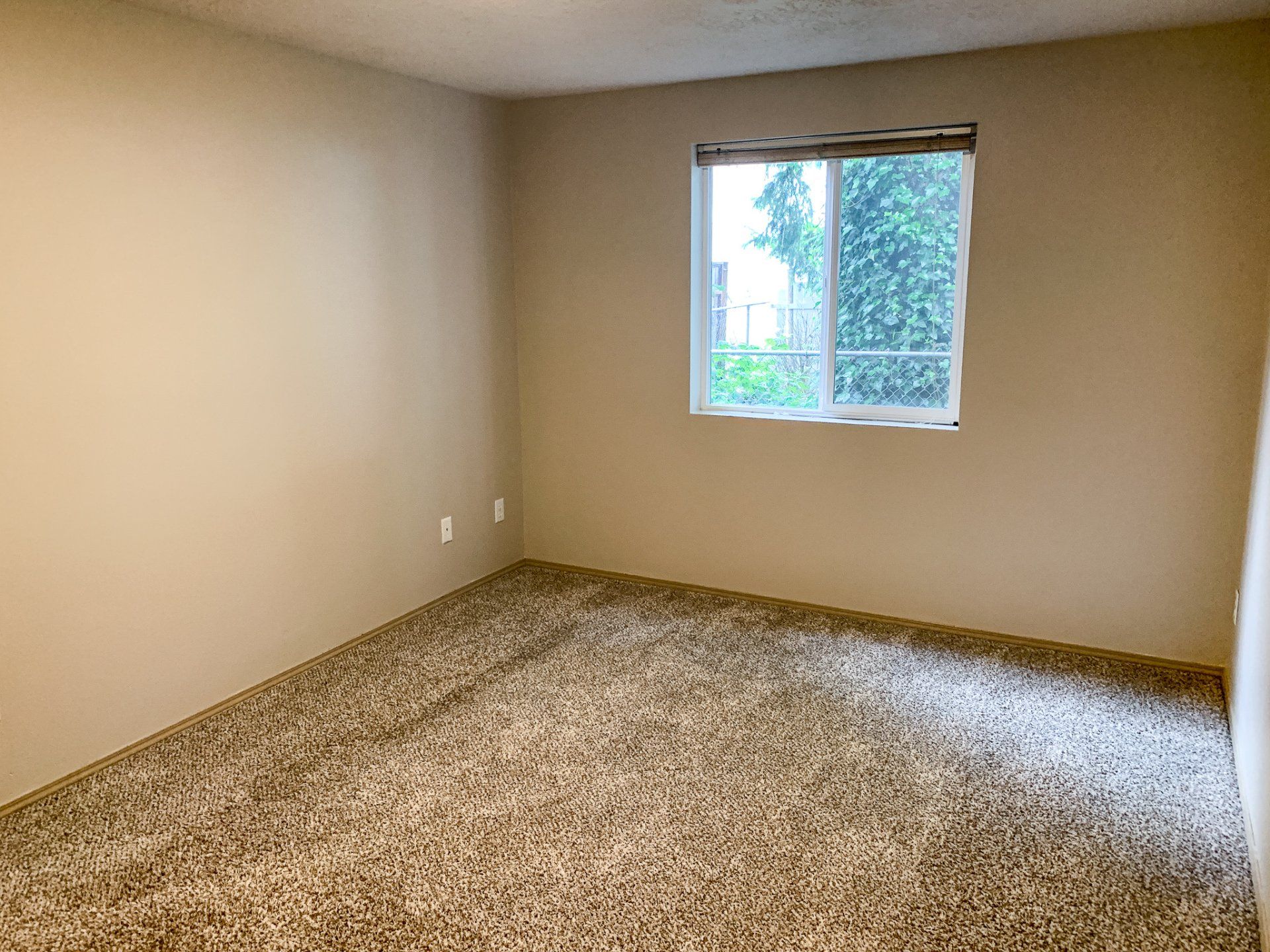 An empty bedroom with a carpeted floor and a window.