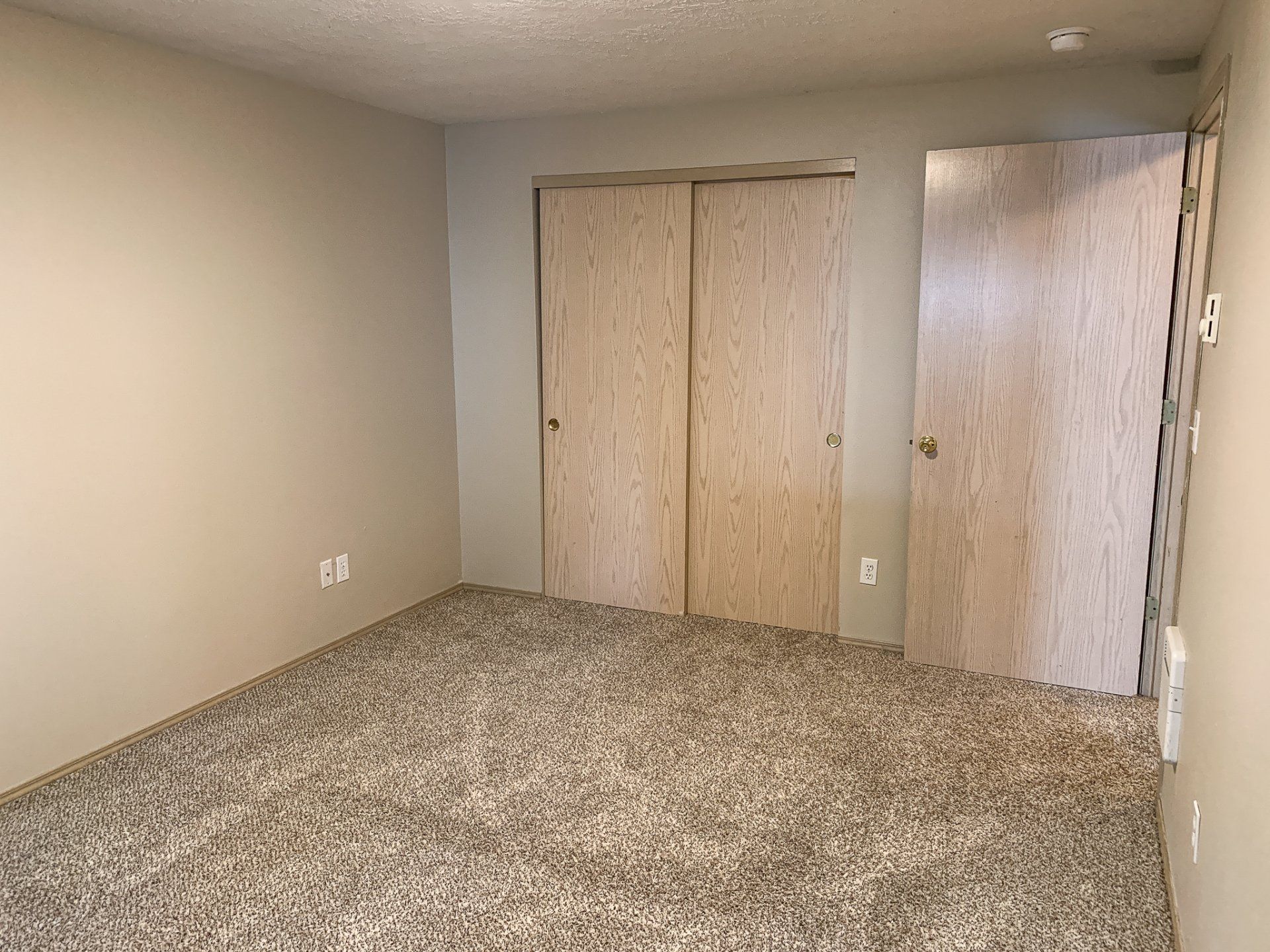 An empty bedroom with a carpeted floor and two closets.