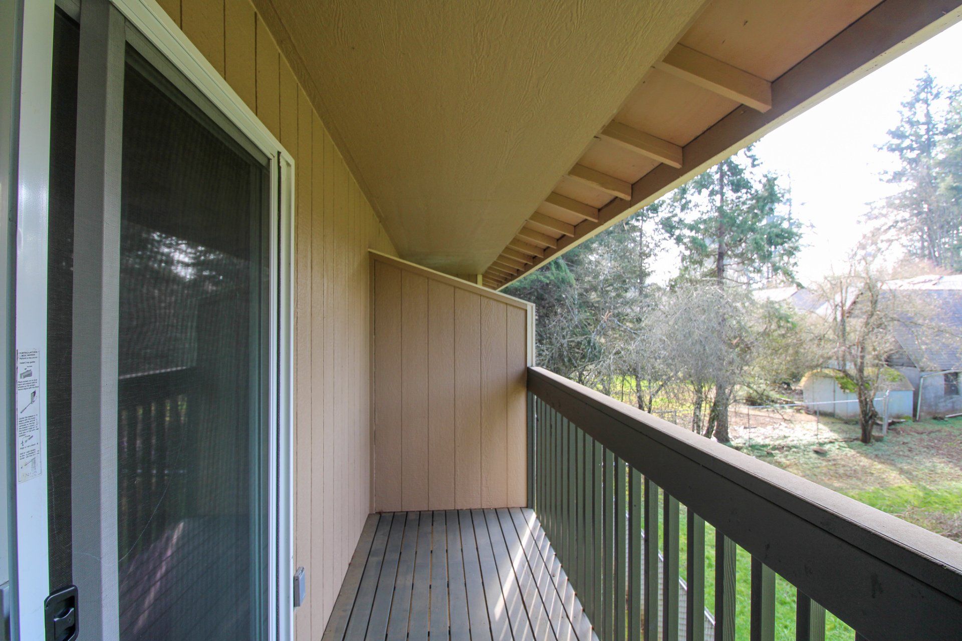 An empty balcony with a sliding glass door and trees in the background