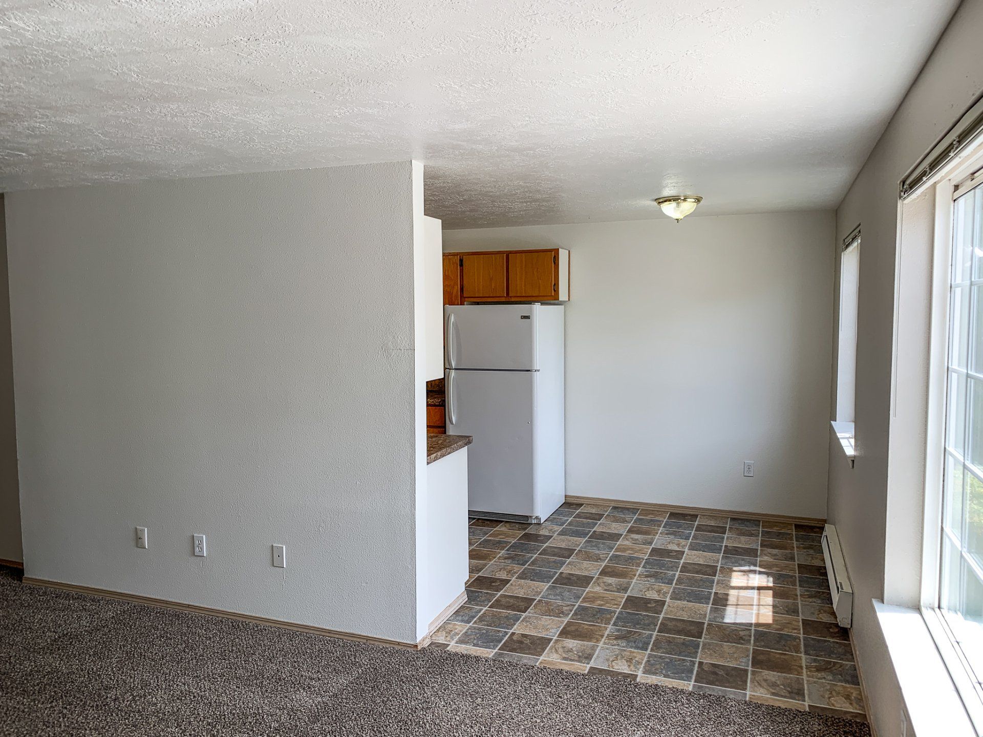 An empty living room with a tiled floor and a refrigerator