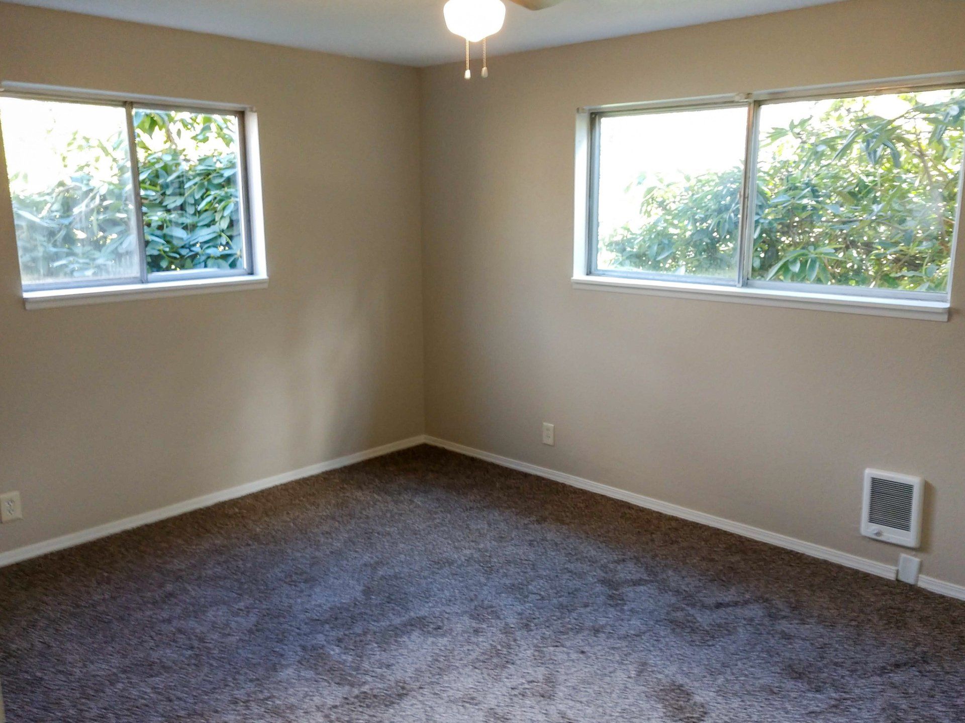 An empty bedroom with two windows and a ceiling fan.