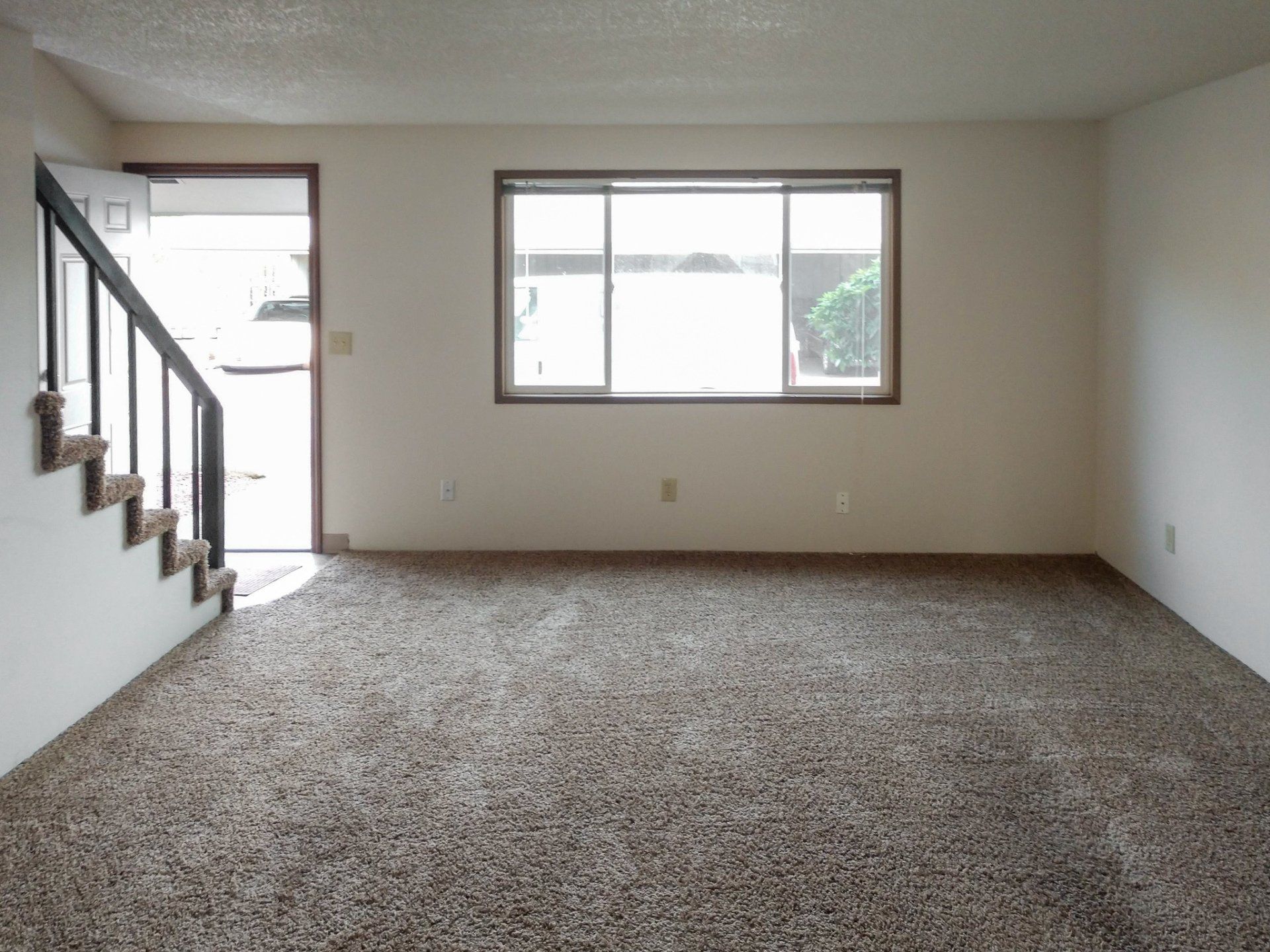 An empty living room with stairs and a window