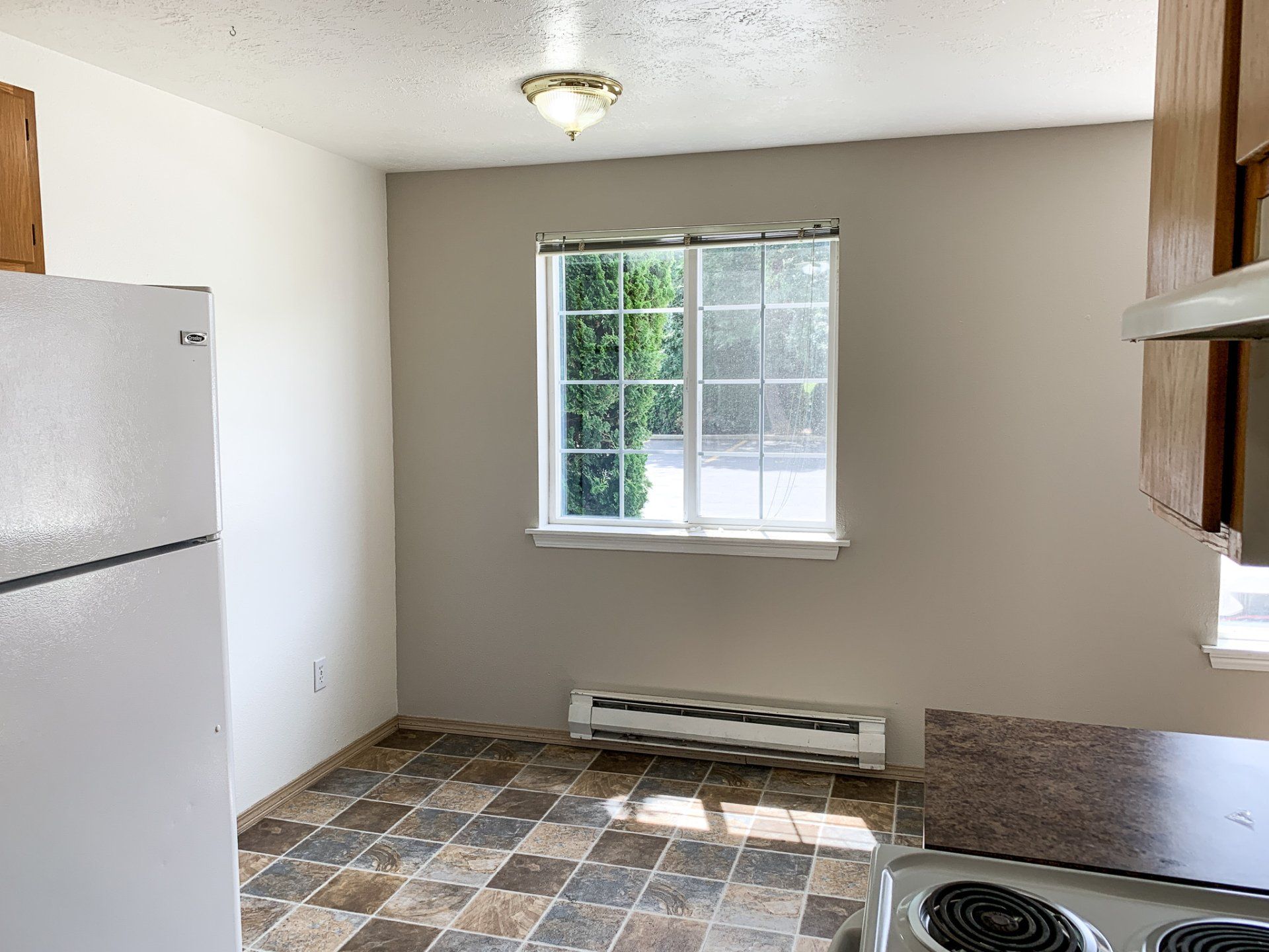 An empty kitchen with a refrigerator , stove , and window.