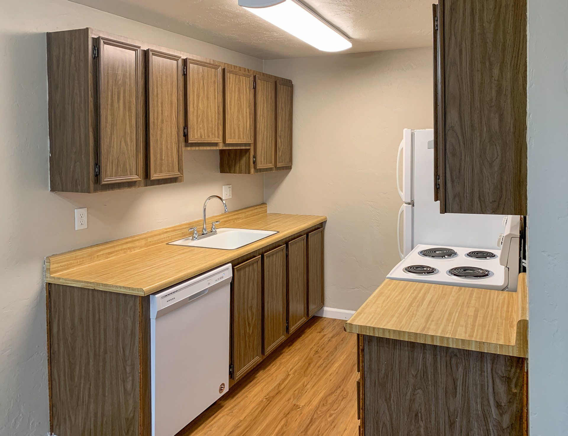 A kitchen with wooden cabinets , a stove , a refrigerator , and a sink.