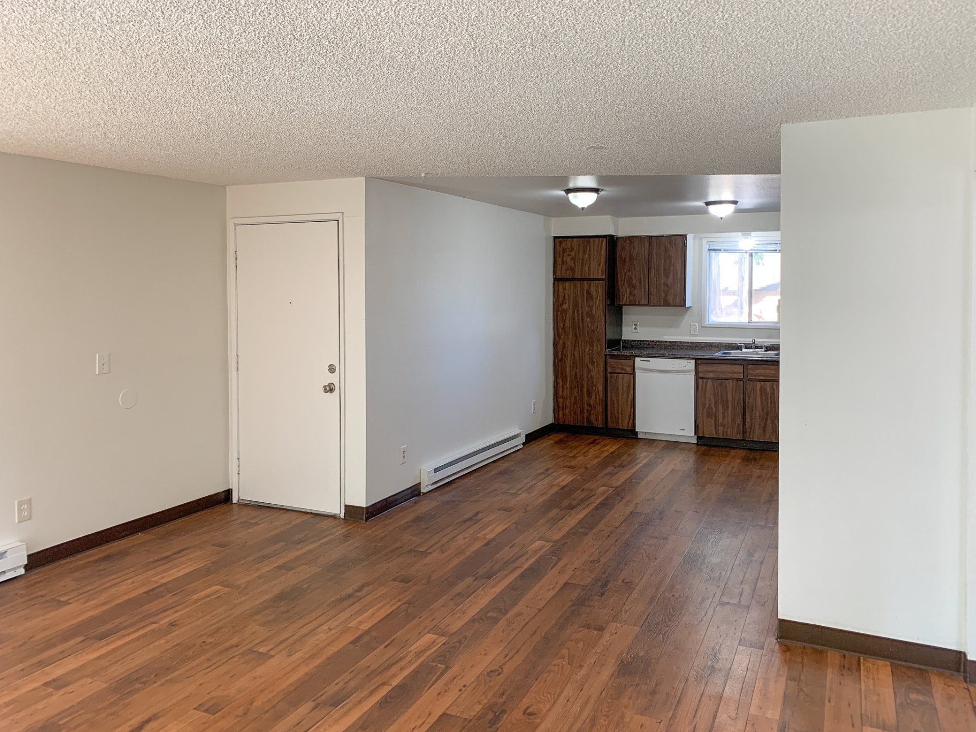A living room with hardwood floors and a kitchen in the background