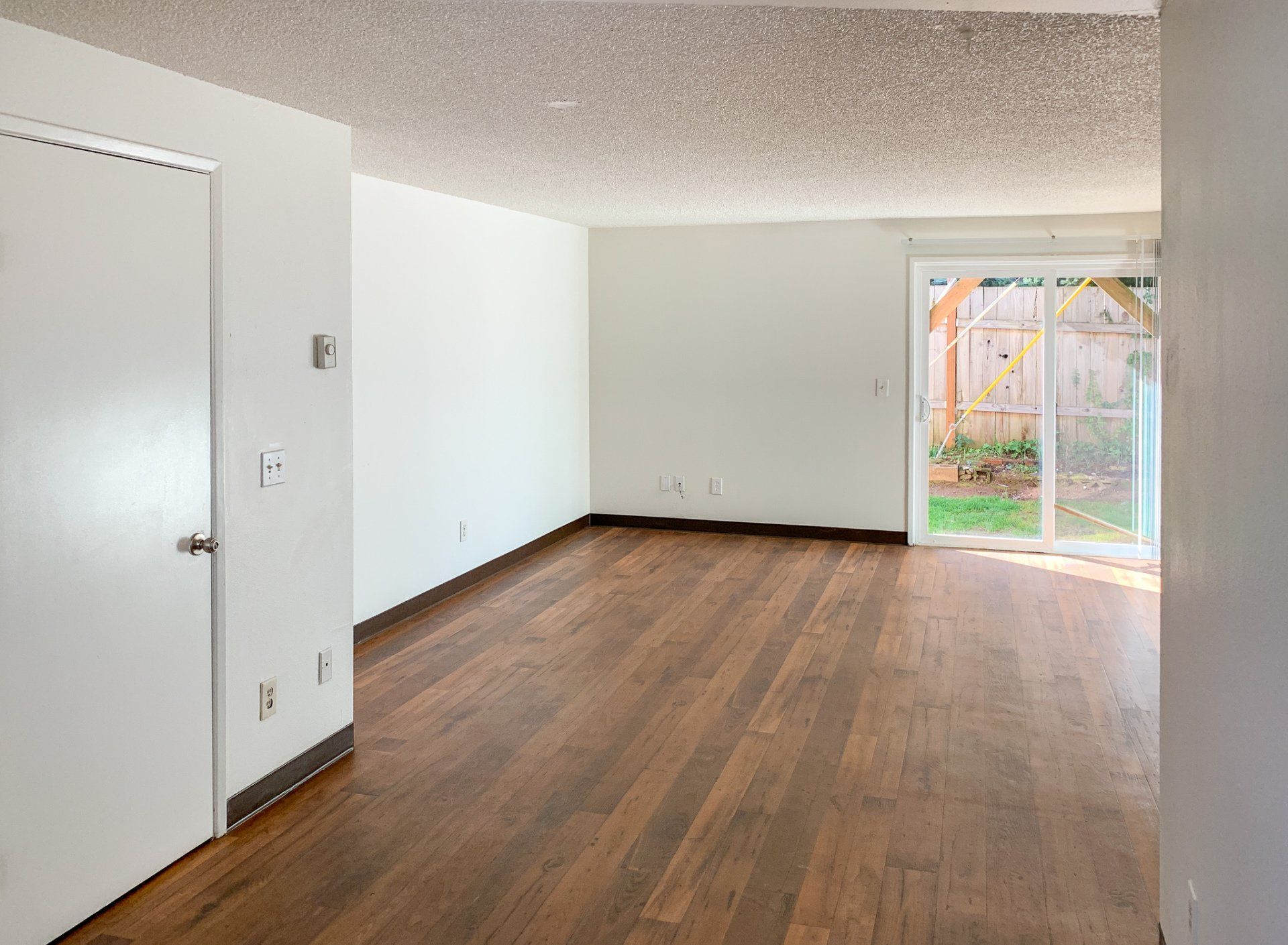 An empty living room with hardwood floors and white walls