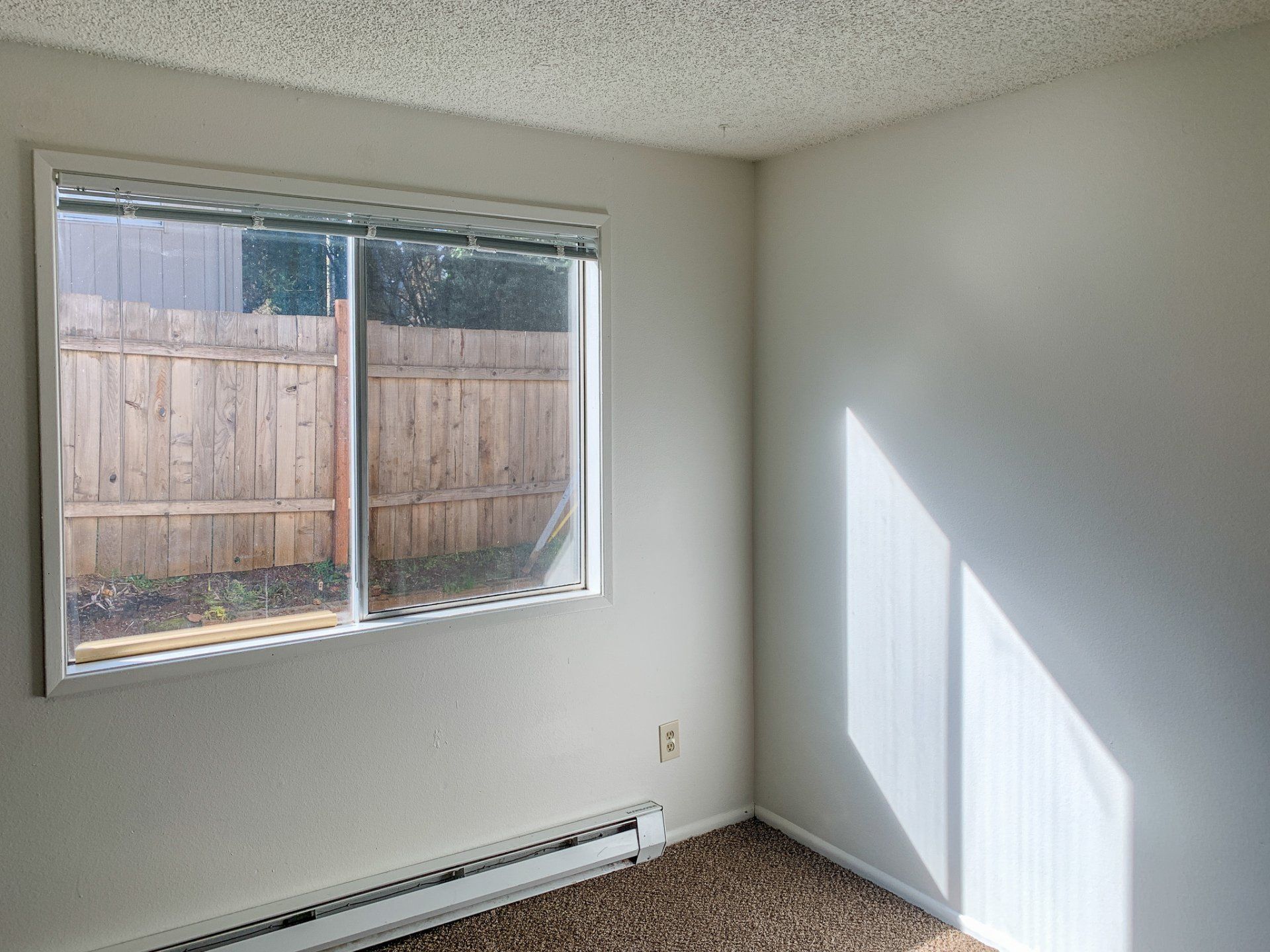 An empty room with a window and a wooden fence in the background.