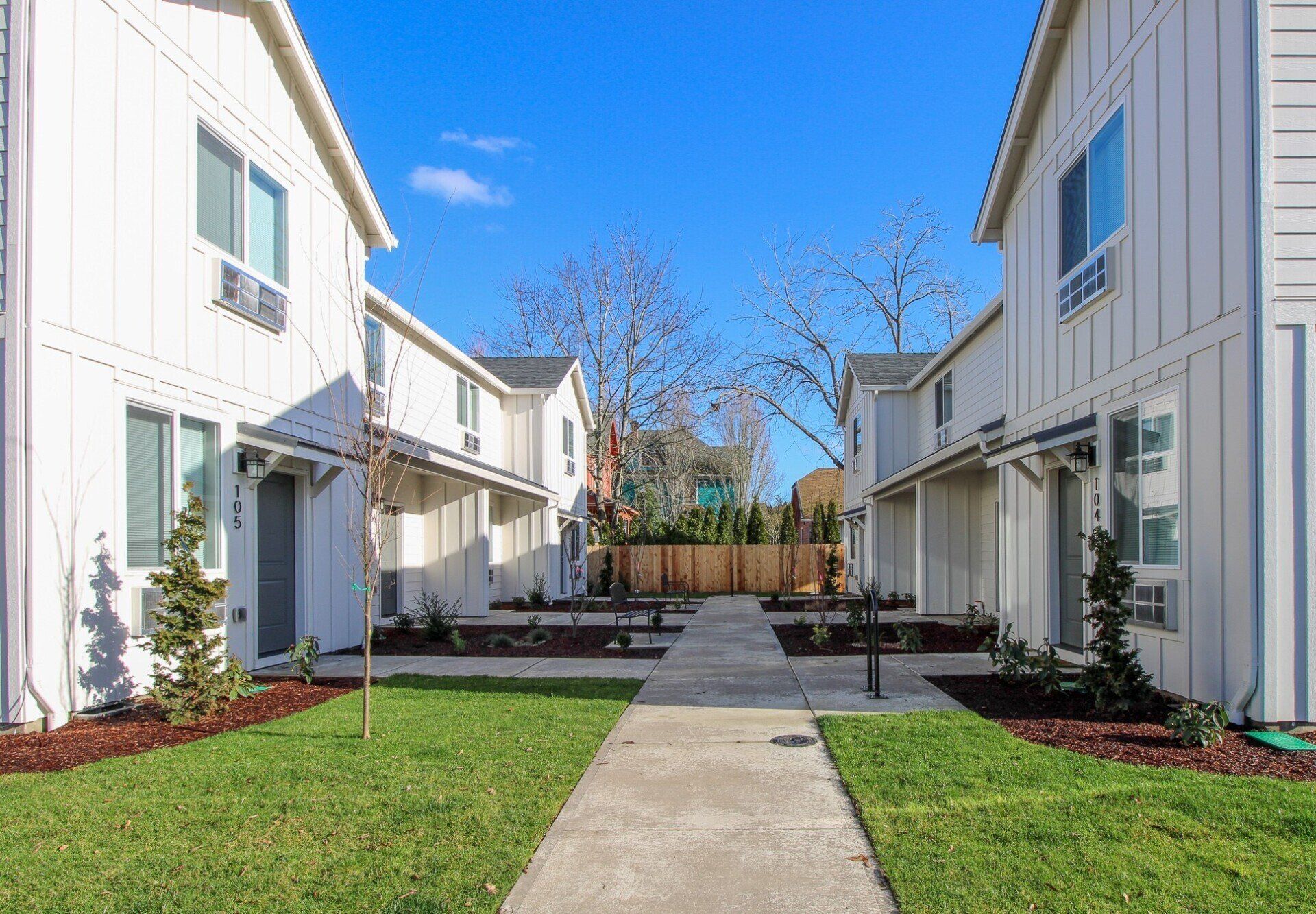 A row of white houses with a concrete walkway between them.