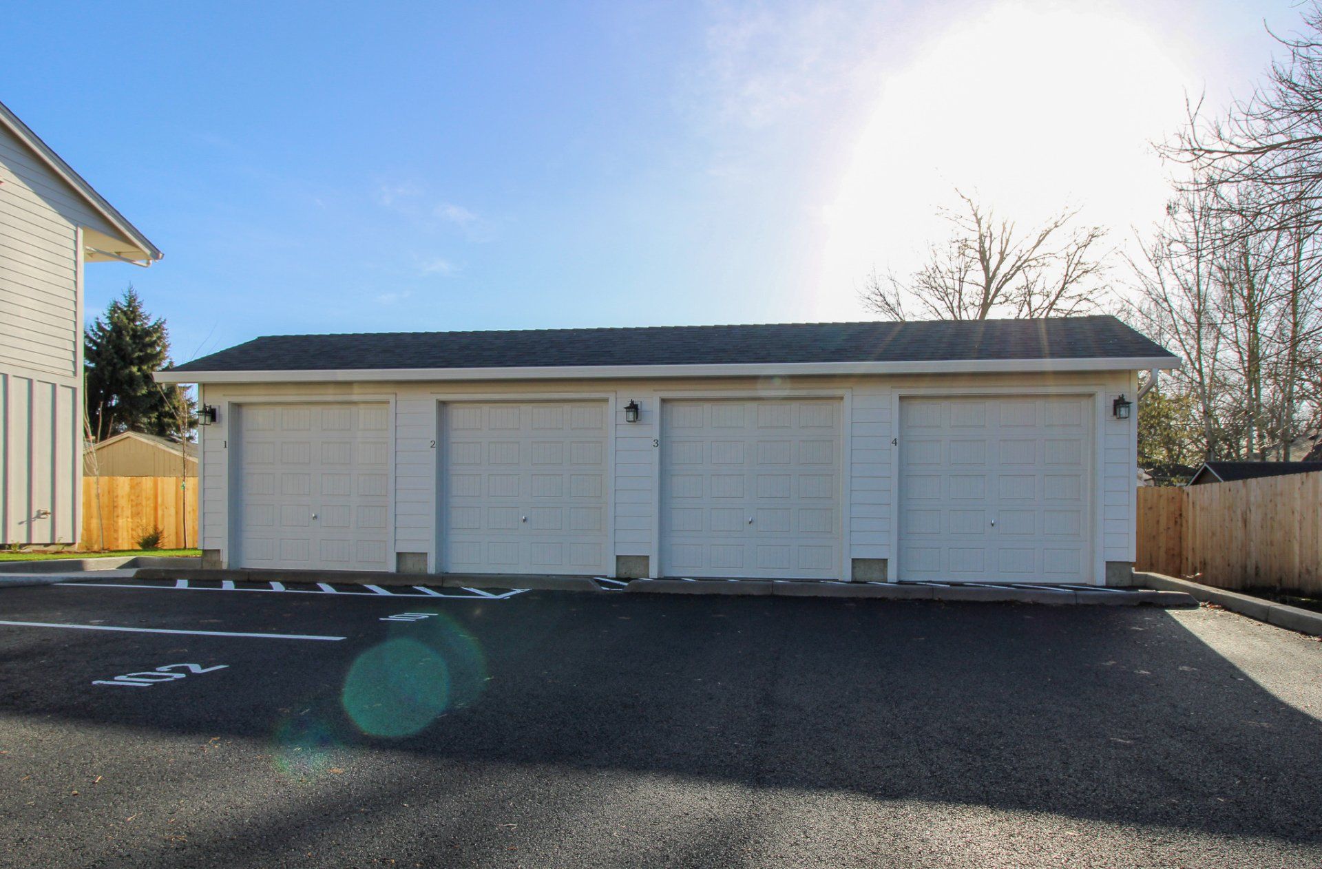 A white garage with a black roof is in a parking lot next to a house.