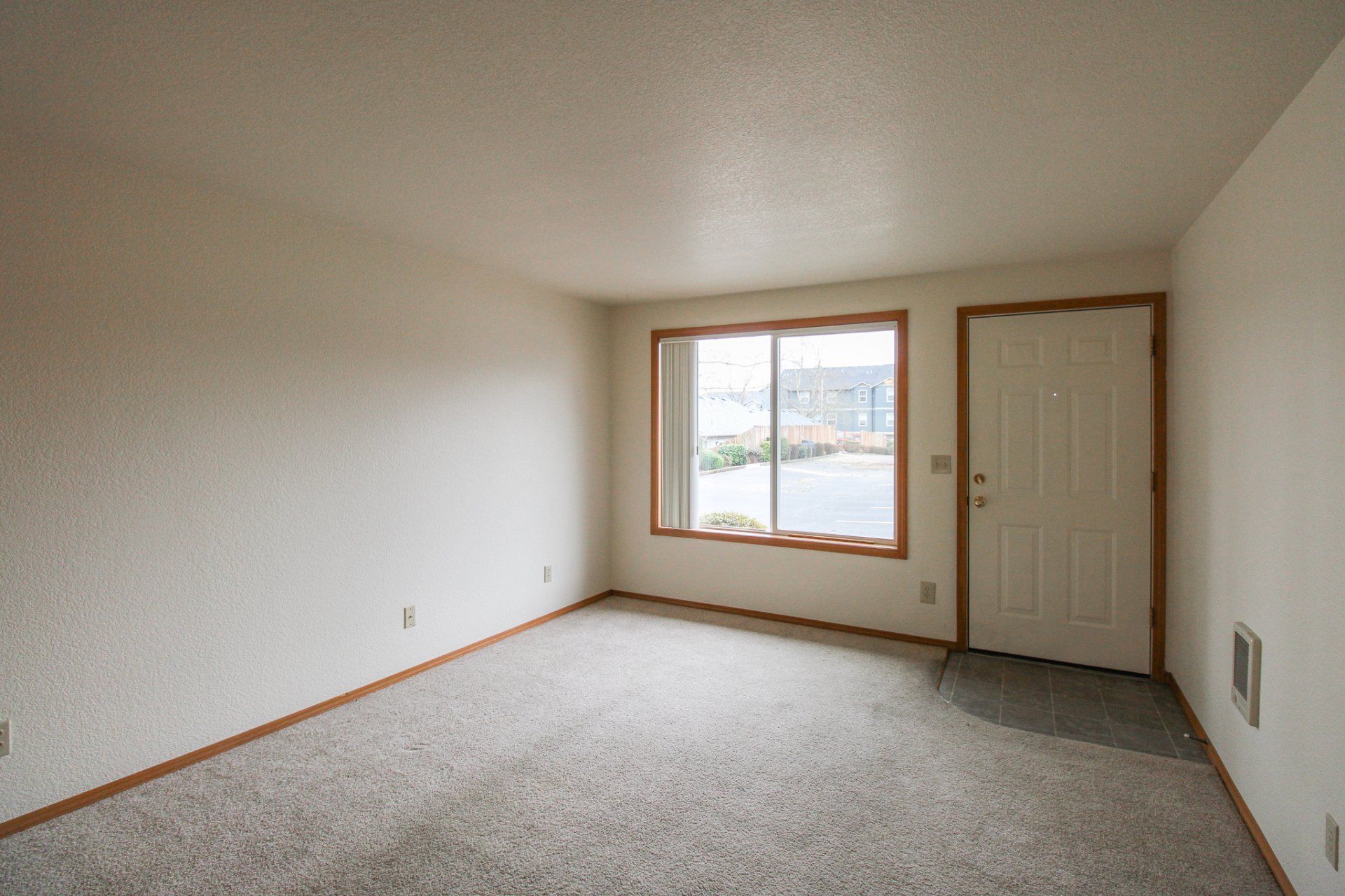 An empty living room with a large window and a door.