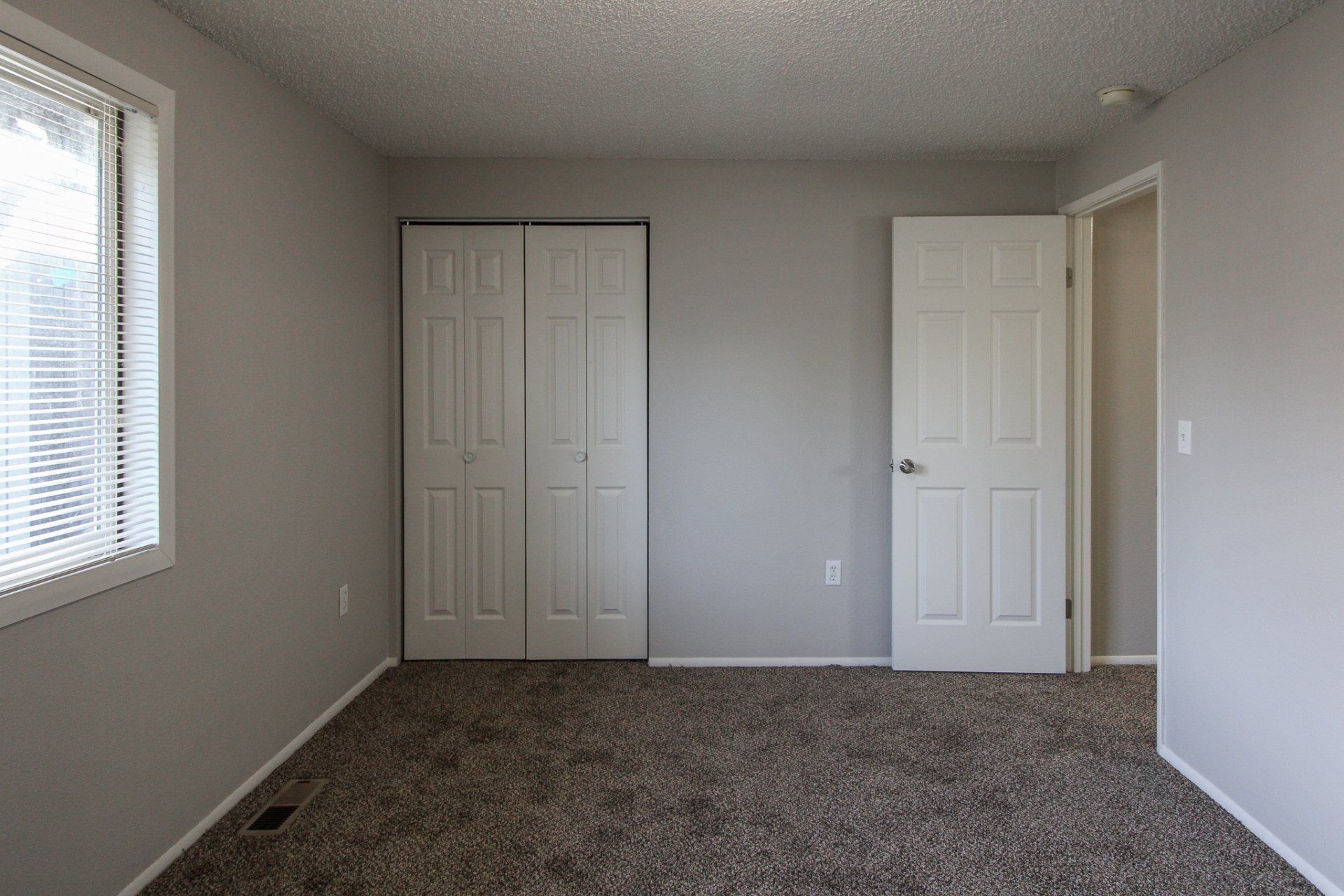 An empty bedroom with a closet and a window.