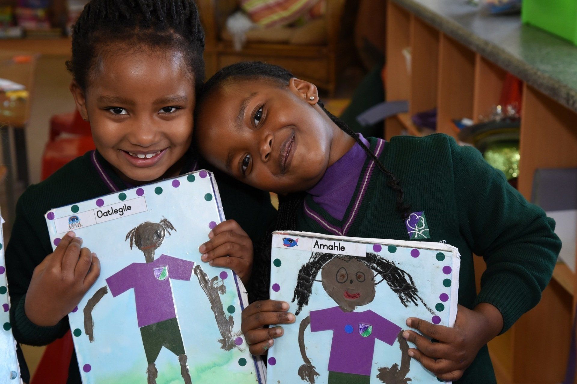 two young girls are holding up their drawings and smiling for the camera .
