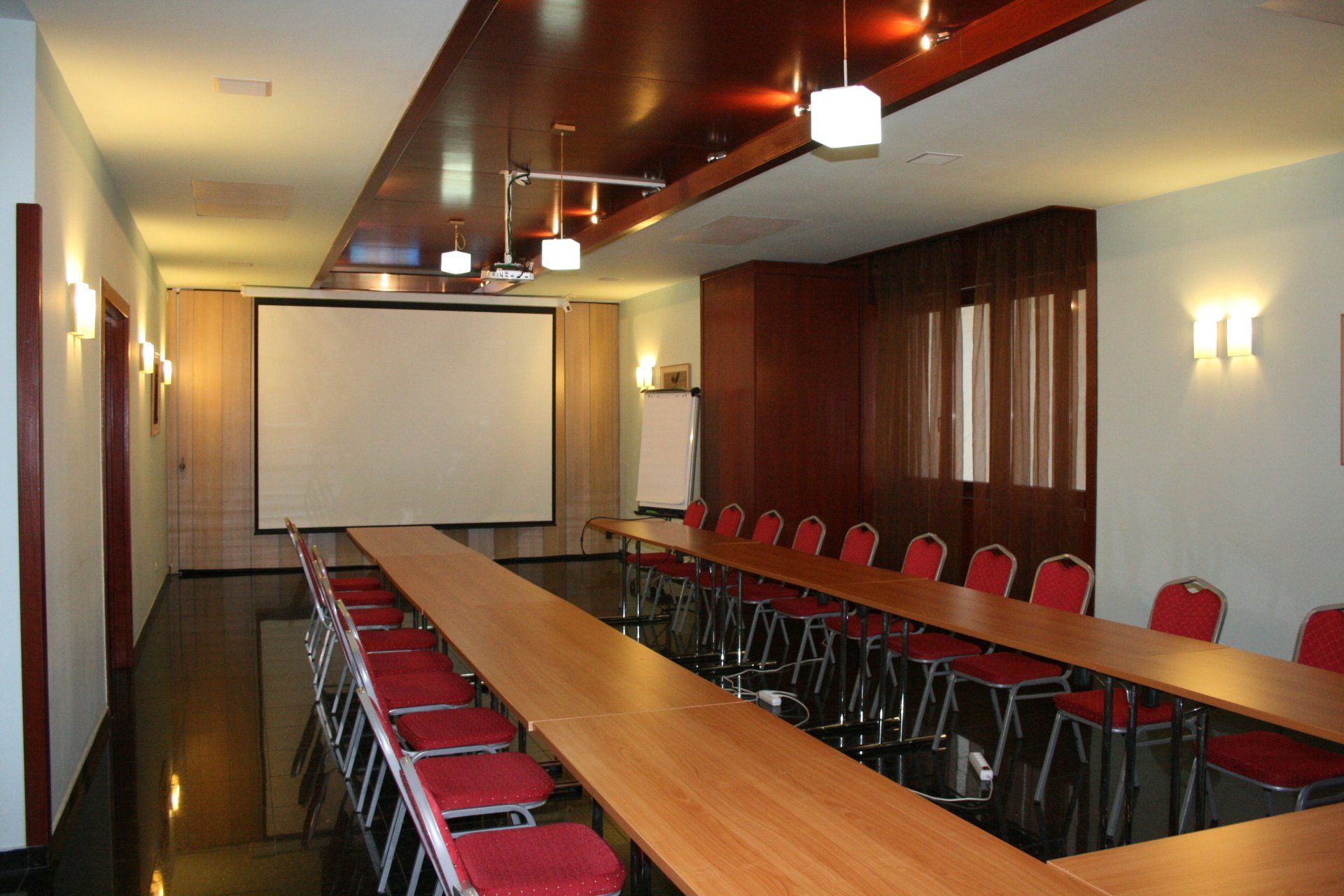 A conference room with long tables and chairs and a projector screen