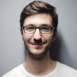 A man wearing glasses and a white shirt is smiling for the camera.