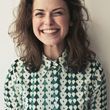 A woman wearing a green and white checkered shirt is smiling