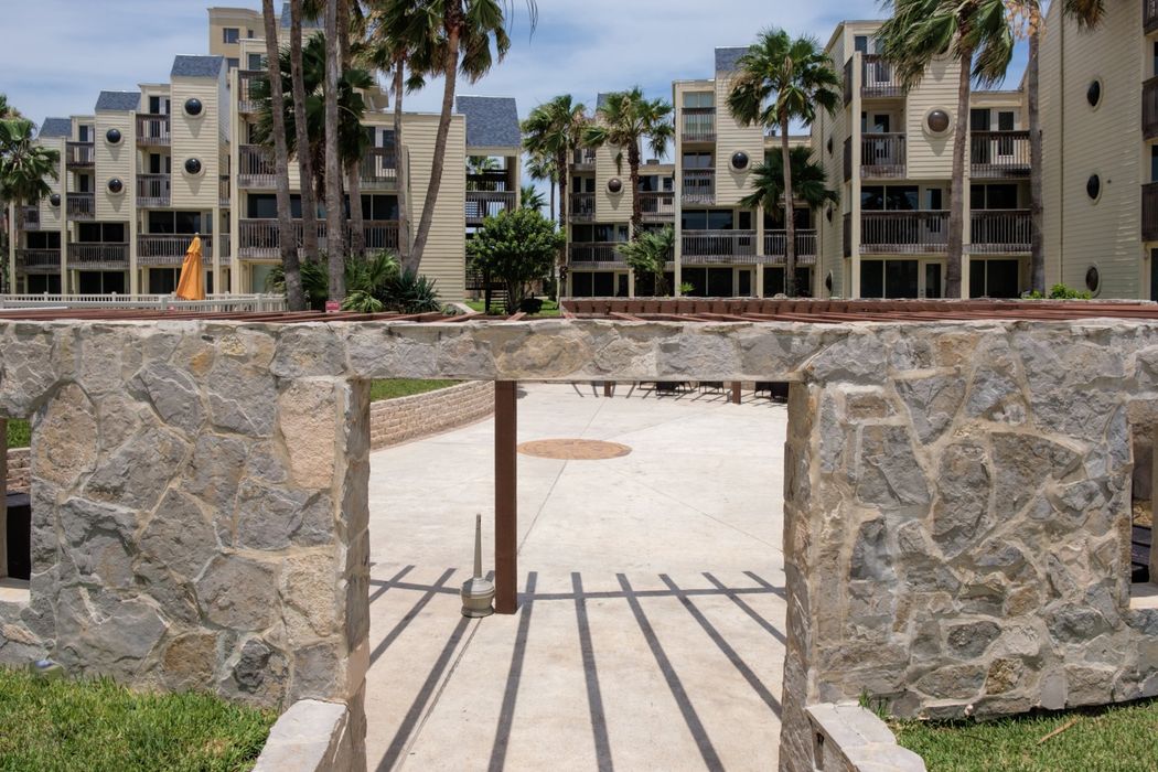 Un arco de piedra que conduce a un edificio con palmeras al fondo.